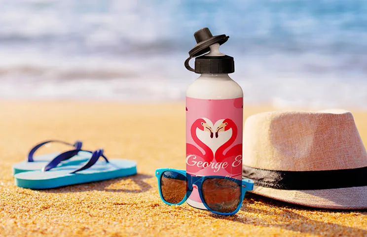 Personalised flamingo water bottle on sandy beach, next to sunglasses & hat.  Perfect summer gift!